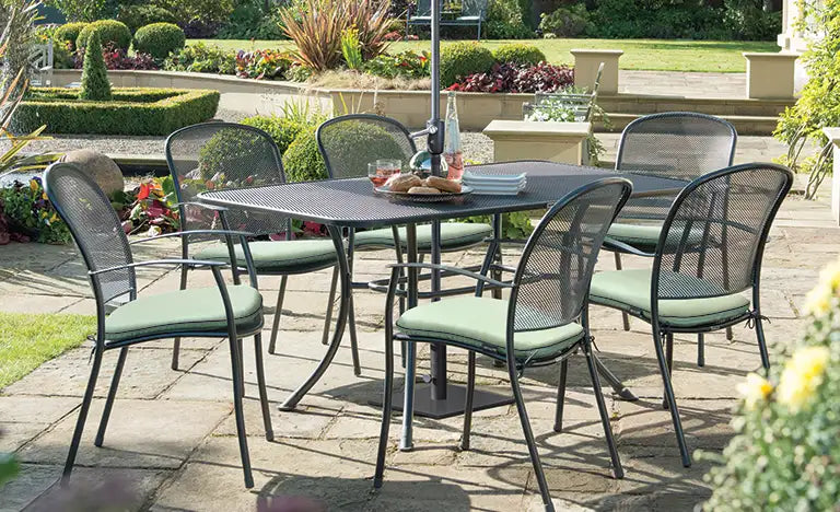 Outdoor metal dining table with six mesh chairs on a garden patio.