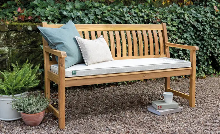 Wooden garden bench with cushions on a gravel patio.