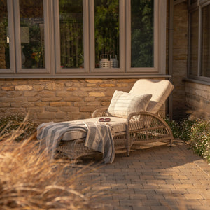 Sahara wicker sun lounger with cushions on a patio area in front of a stone wall.