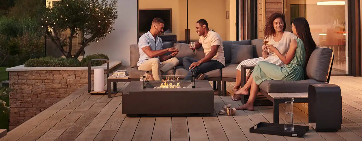 men and women sitting in front of a fire pit drinking