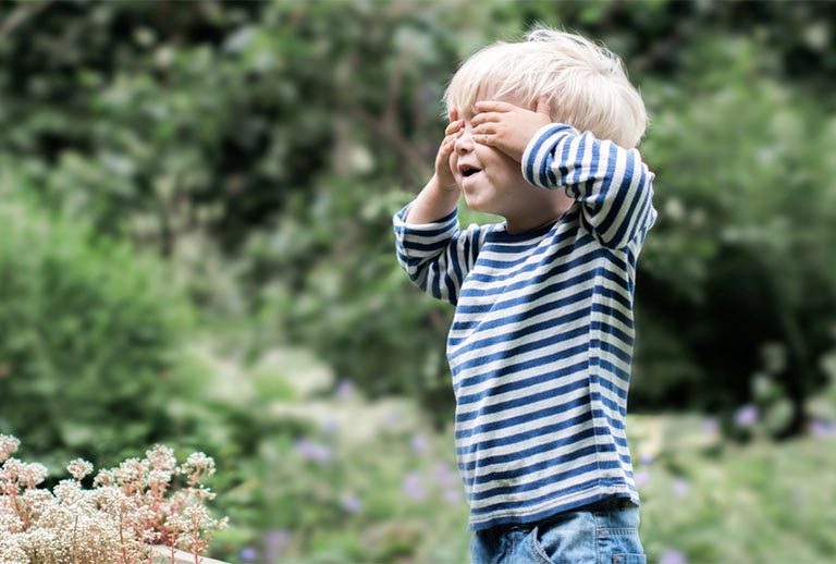 Young boy in a striped sweater holding his eyes closed for a game of hide and seek.