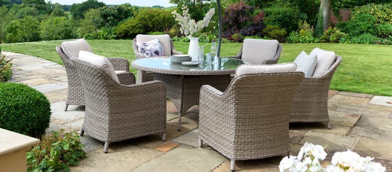 Kettler's Charlbury Round Dining Set on a slated patio in front of a big lawn.