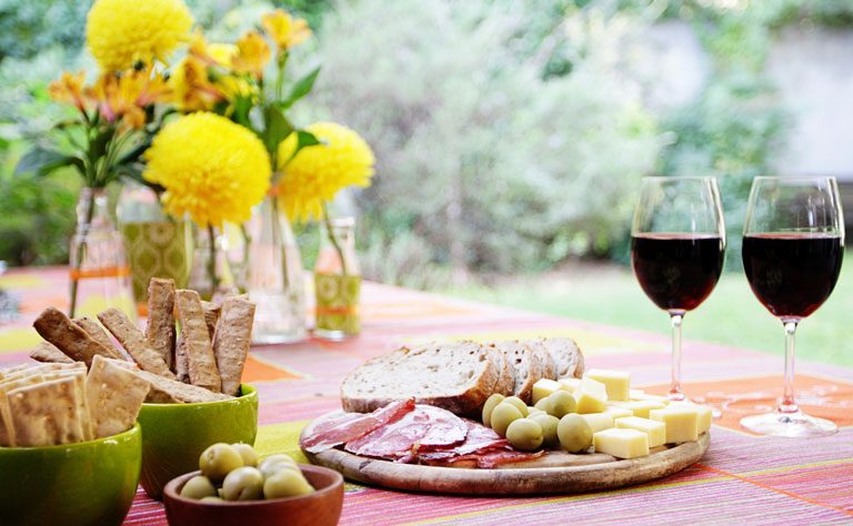 Garden party table with tapas, breadsticks, red wine and yellow flowers.