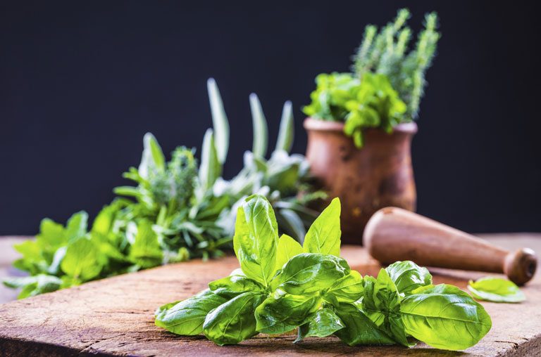 Basil and other herbs on and next to a chopping board.