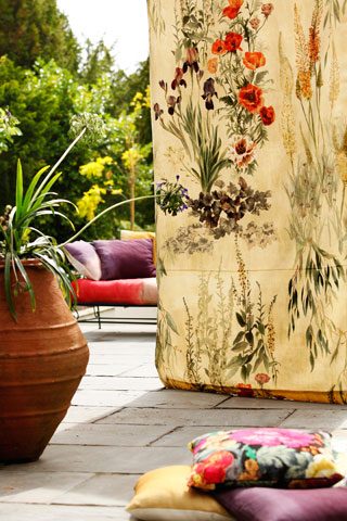 Garden patio decked out with sofa, colourful cushions and floral materials.