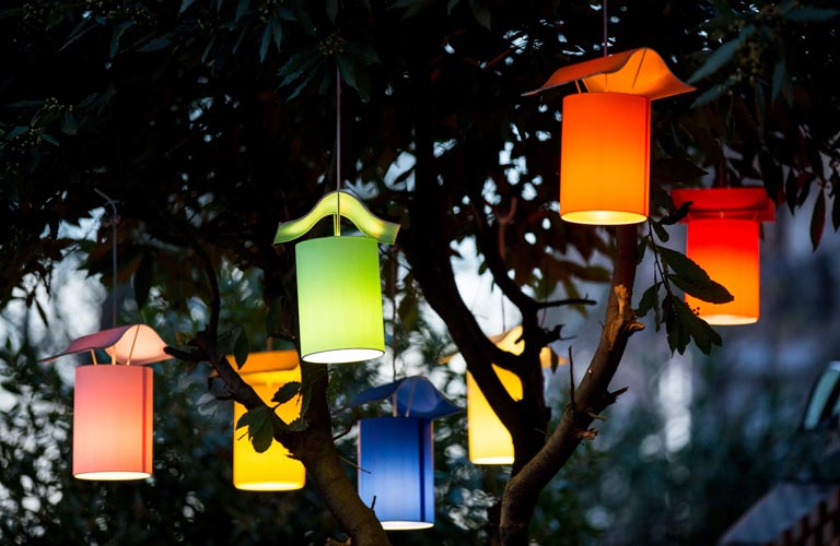 Seven colourful, lit lanterns hanging in garden tree