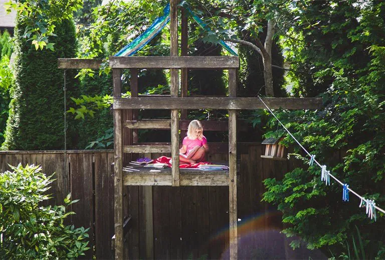 Blonde girl reading in a wooden treehouse.