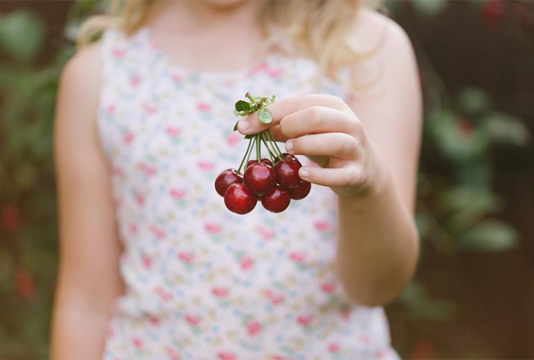 Blonde girl holding a bundle of cherries.