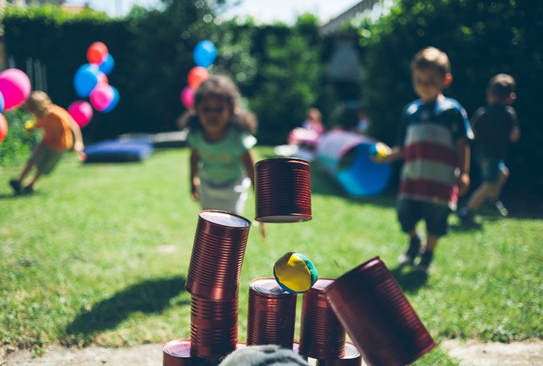 Children playing can toss game in garden.