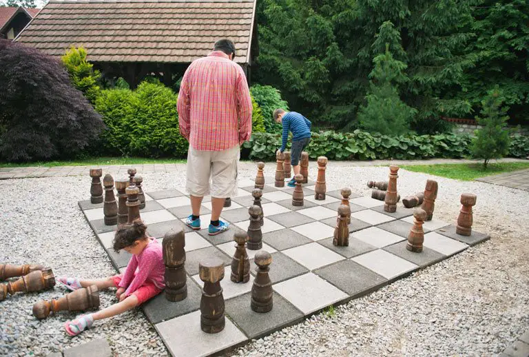 Man playing large outdoor chess game with boy.