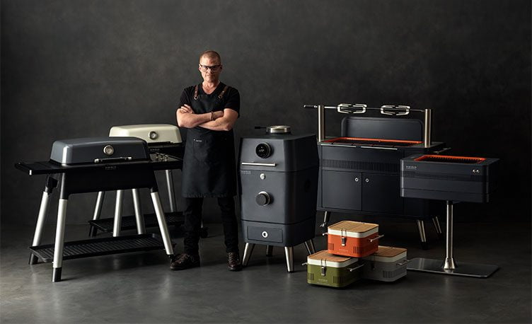 Heston Blumenthal standing in front of the full range of Everdure by Heston Blumenthal BBQ's.