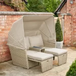 Palma daybed in oyster with gstone cushions with hood up and seats in extended position in the garden agains a brick wall