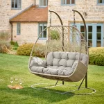 Palma double cocoon swinging seat in oyster wicker in a garden on the grass in front of a hoouse
