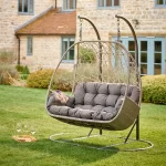 Palma double cocoon swinging seat in white wash wicker in a garden on the grass in front of a hoouse