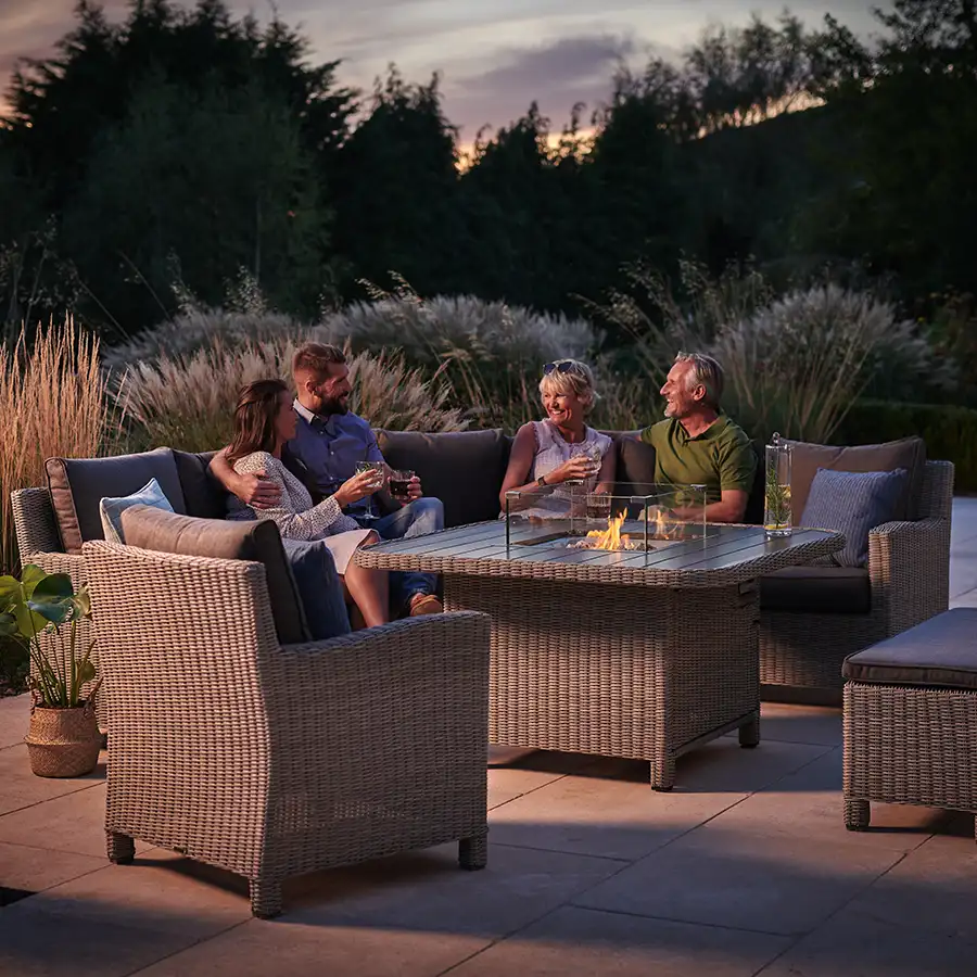 Family sat around a Palma grande casual dining corner set with fire pit lit in on a summers evening in the garden