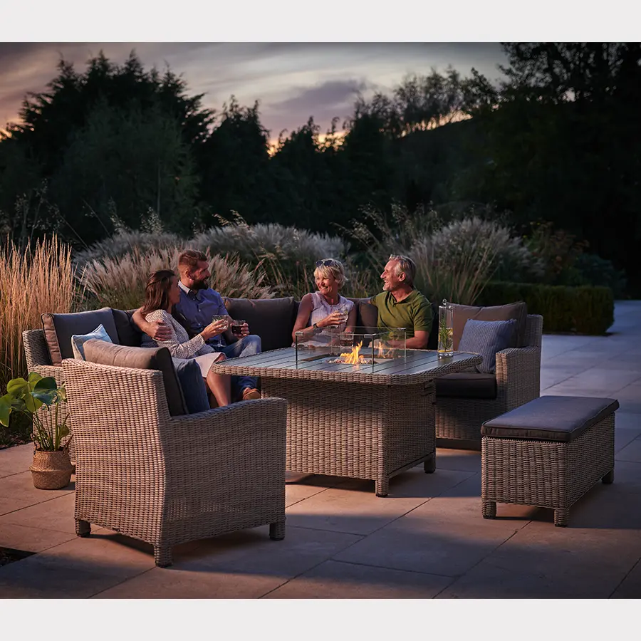 Family sat around a Palma grande casual dining corner set with fire pit lit in on a summers evening in the garden