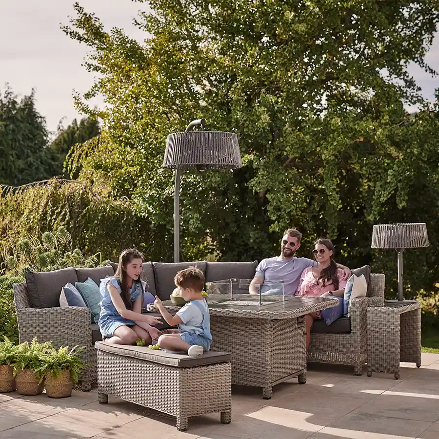 Family sat around a Palma grande casual dining corner set with fire pit lit in on a summers day in the sunshine