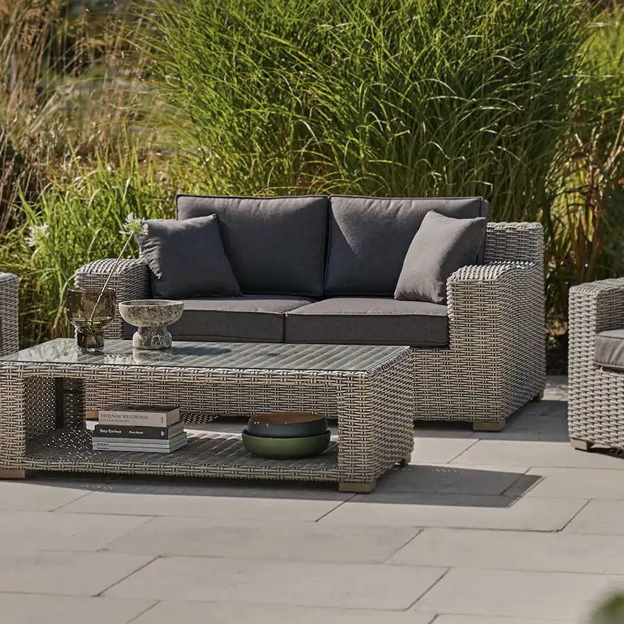 Palma luxe 2 seater sofa in white wash wicker with grey cushions on a garden patio next to a coffee table