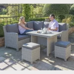 Couple sat on a Palma mini corner sofa set with dark oak slat top ploywood table in the garden with sunshine