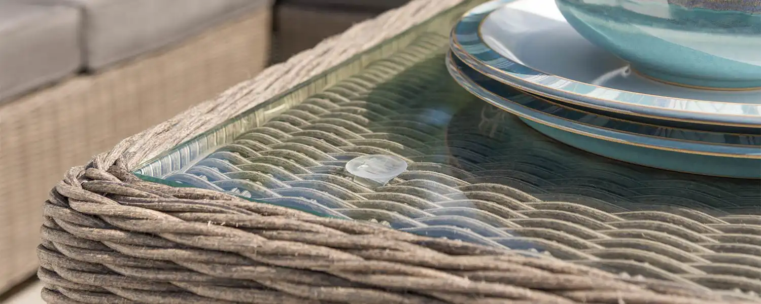 Close up of a glass table top on wicker garden furniture.