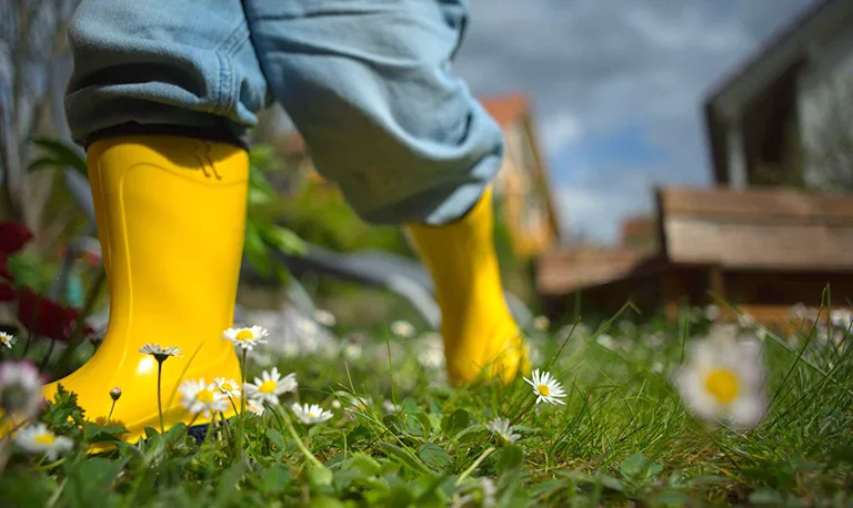 Child runing though grass and daisys in yellow wellies