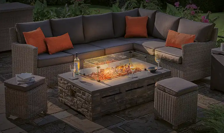 Firepit table glowing next to garden furniture at night time